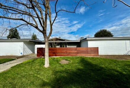A South Pacific Redwood fence in front of a house with a tree in the yard.