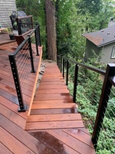 hardwood deck and stairs with cable railings in a forested backyard